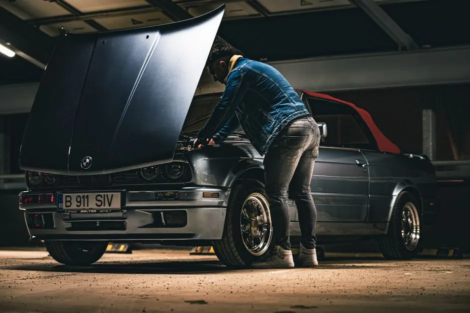 Man working on a convertible car in a garage, checking the engine under the hood.